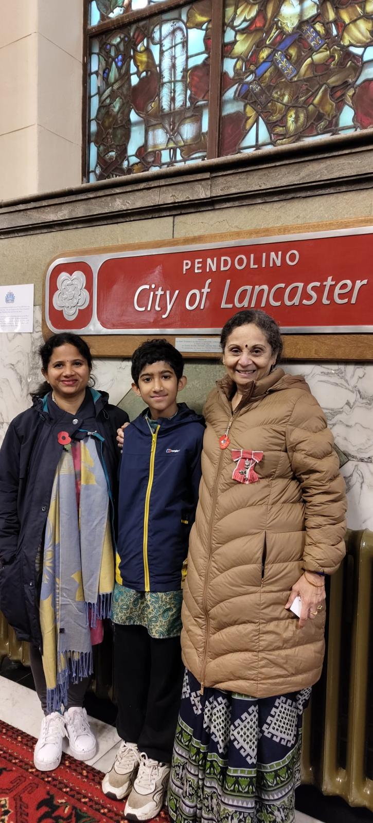 Harsha wearing her MBE with family by the City of Lancaster train nameplate